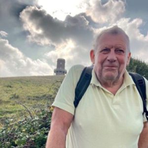 Picture of Ken, a volunteer in Dorset on a hill with a folly behind him in the background