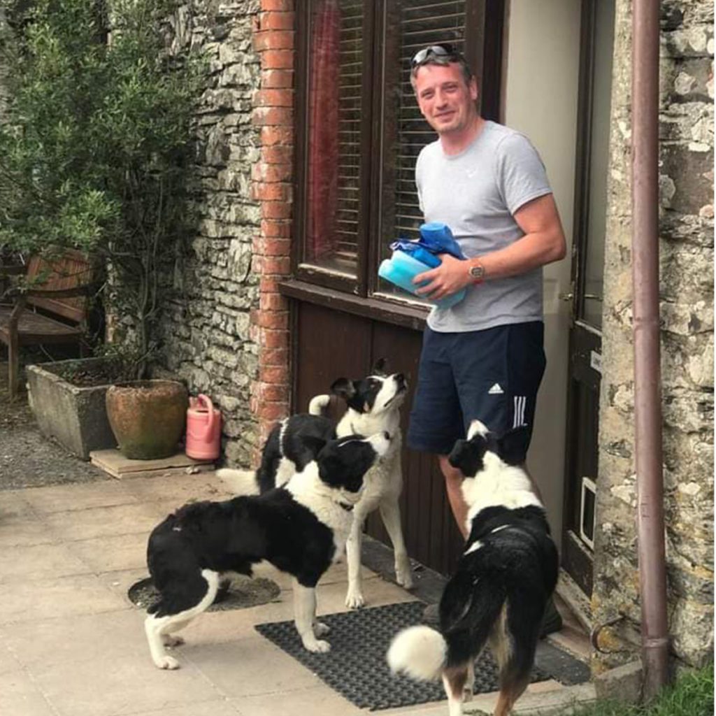 Photo of Adam Hart, Flourish in Nature facilitator outside a cottage with three collie dogs