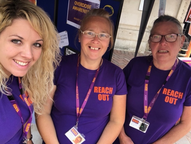 Three Reach workers in branded T shirts next to an information and fundraising stand