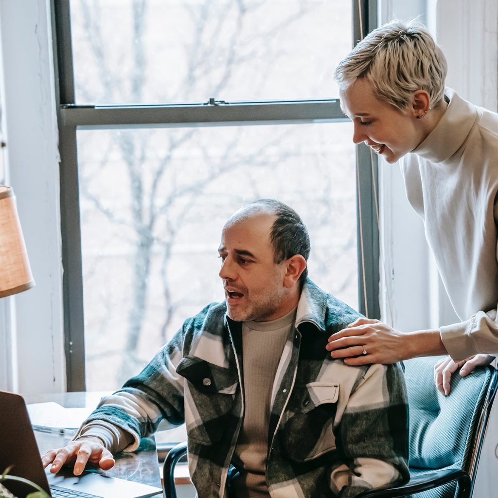 Lady supporting a man in a checked shirt to work on a computer